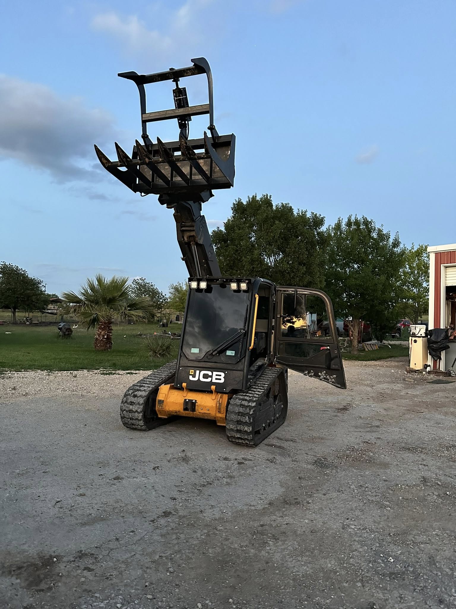 JCB with grapple bucket raised high at golden hour